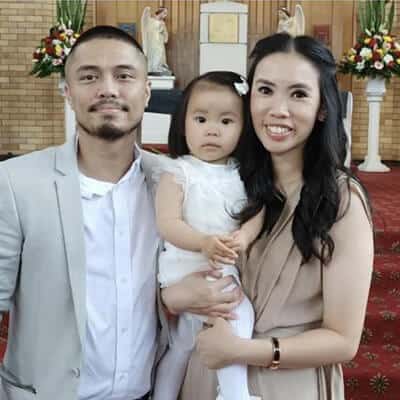 A family of three smiling inside a church; a man, a woman holding a toddler, all dressed in semi-formal attire.